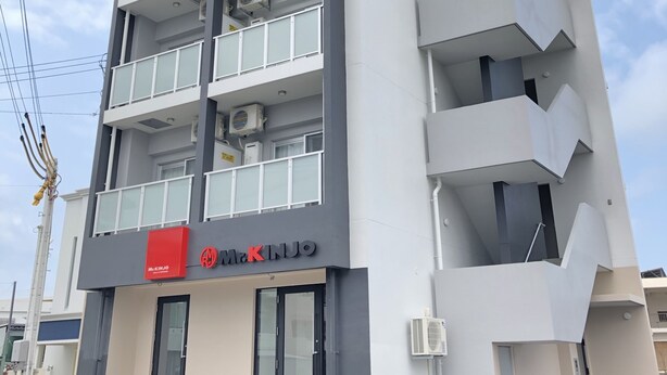 Un edificio de varios pisos con balcones, unidades de aire acondicionado y un letrero rojo con el texto 'McKINJO'.
