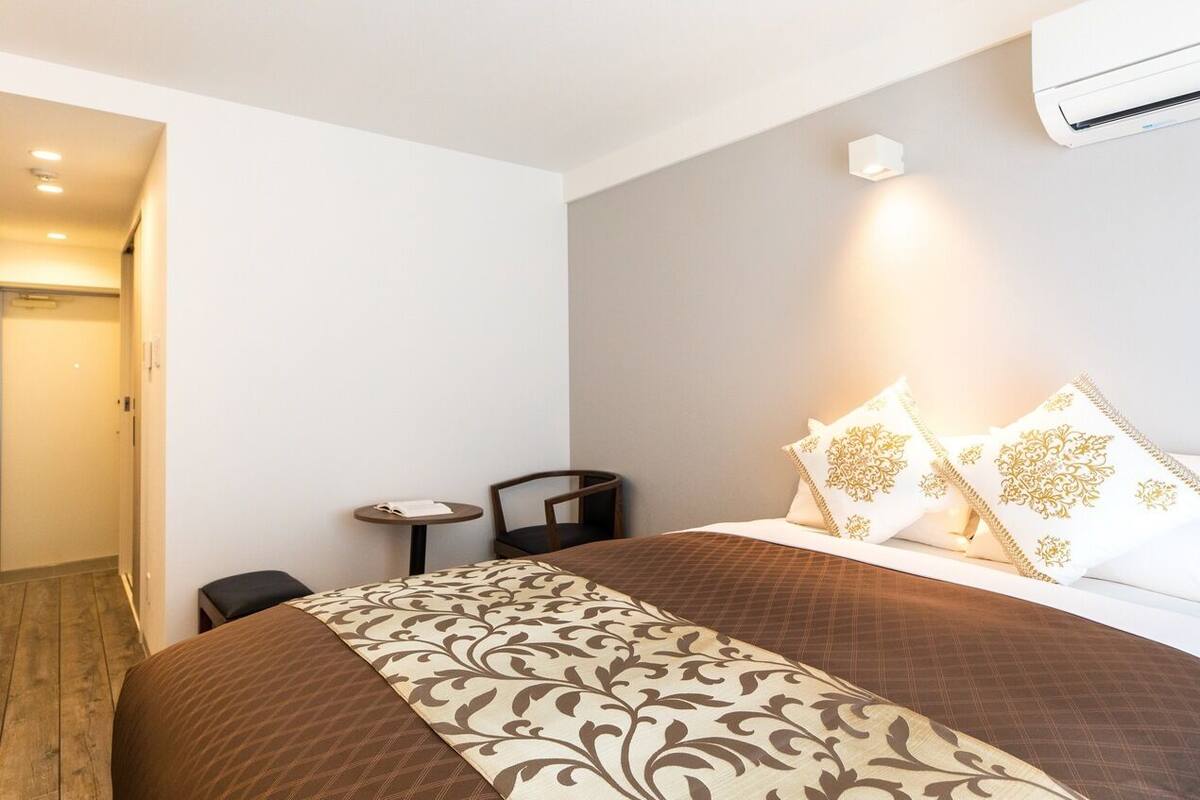 Une chambre d’hôtel avec un lit, une petite table, une chaise et un appareil de climatisation fixé au mur.