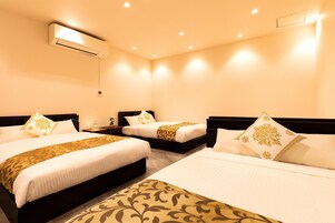 A hotel room with two beds, a wall-mounted air conditioner, and a bedside table with a lamp.