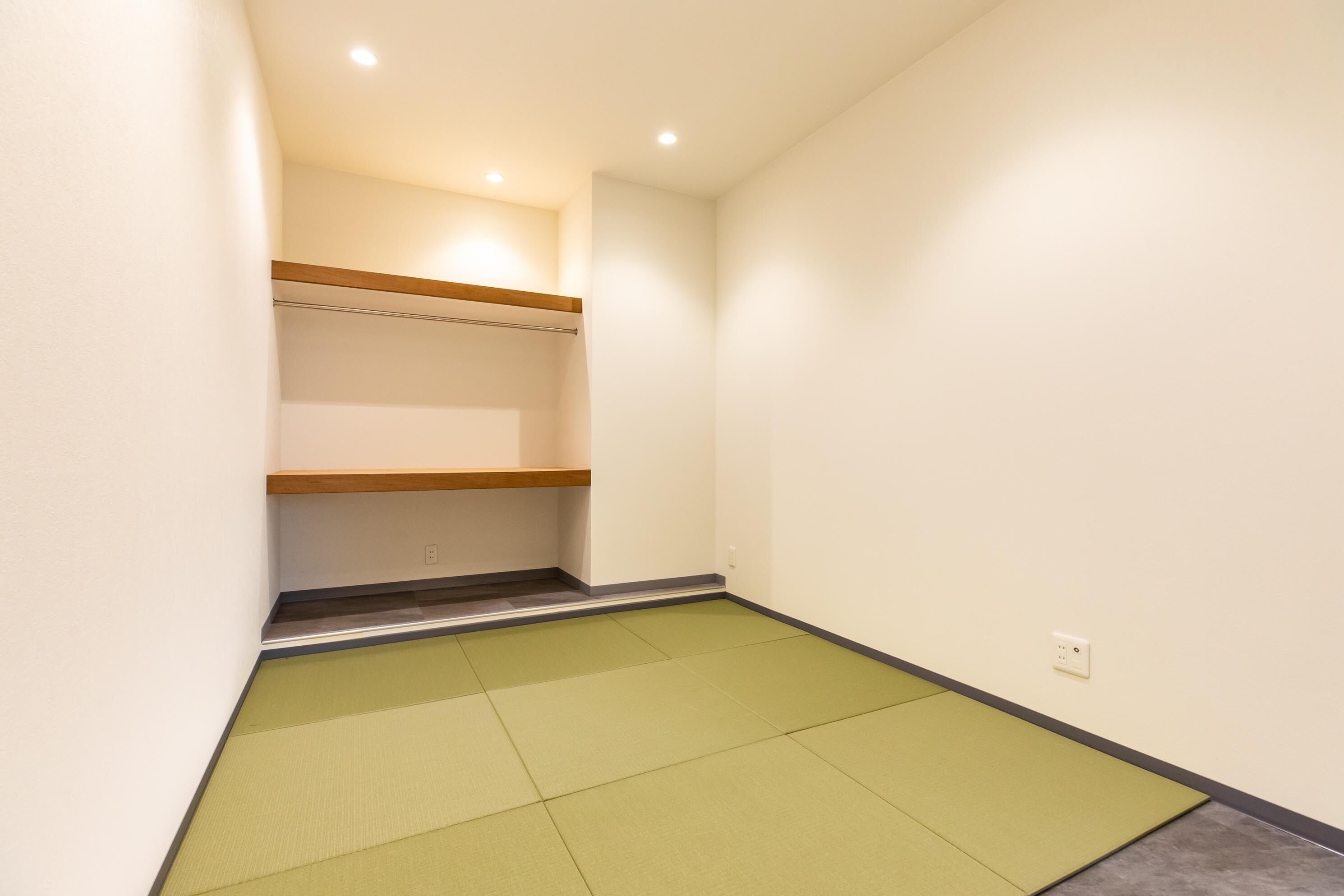 Una habitación con suelo de tatami, estanterías de madera e iluminación empotrada.