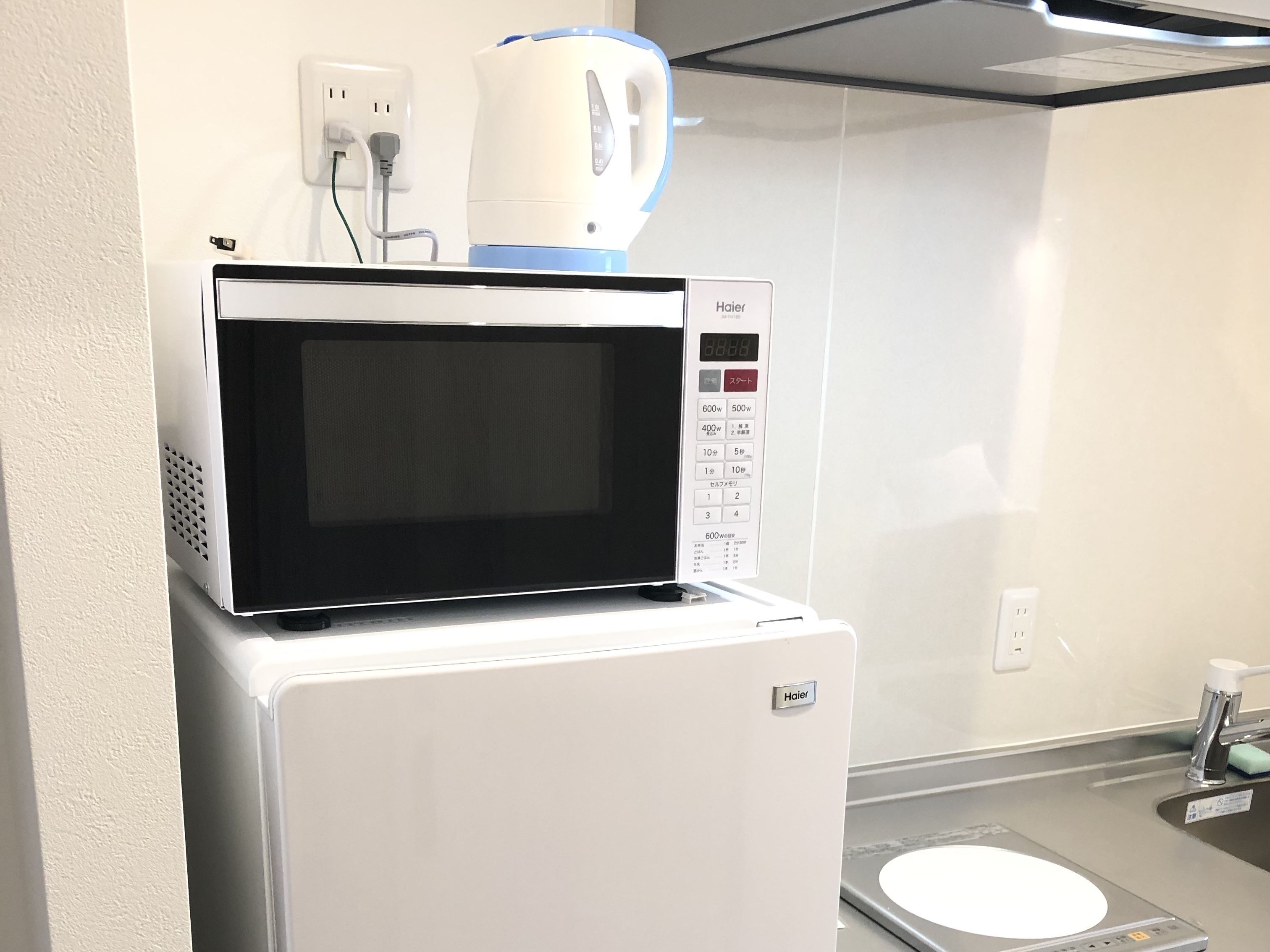 A compact kitchenette with a microwave and a coffee maker on a white refrigerator, a sink, and a small countertop.