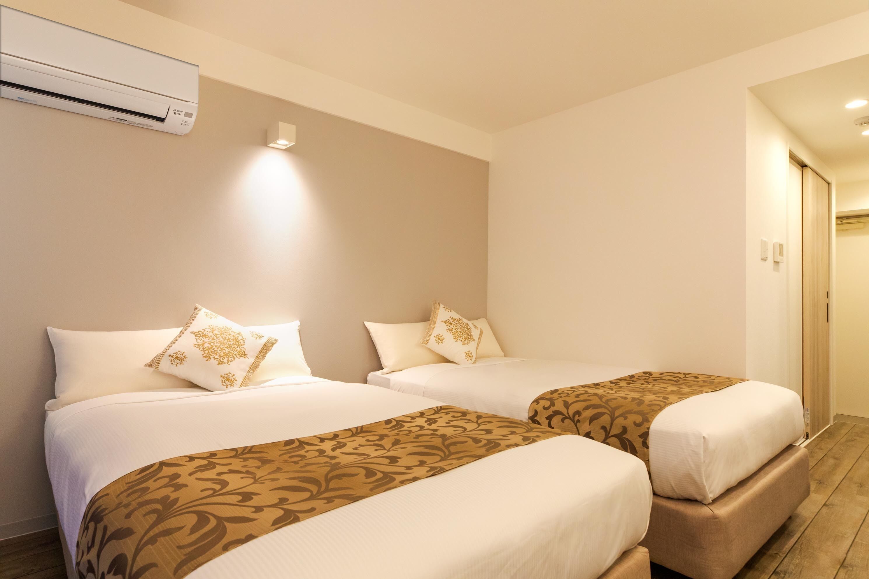 Ein Hotelzimmer mit zwei Betten, beigen Wänden und einem Holzboden.