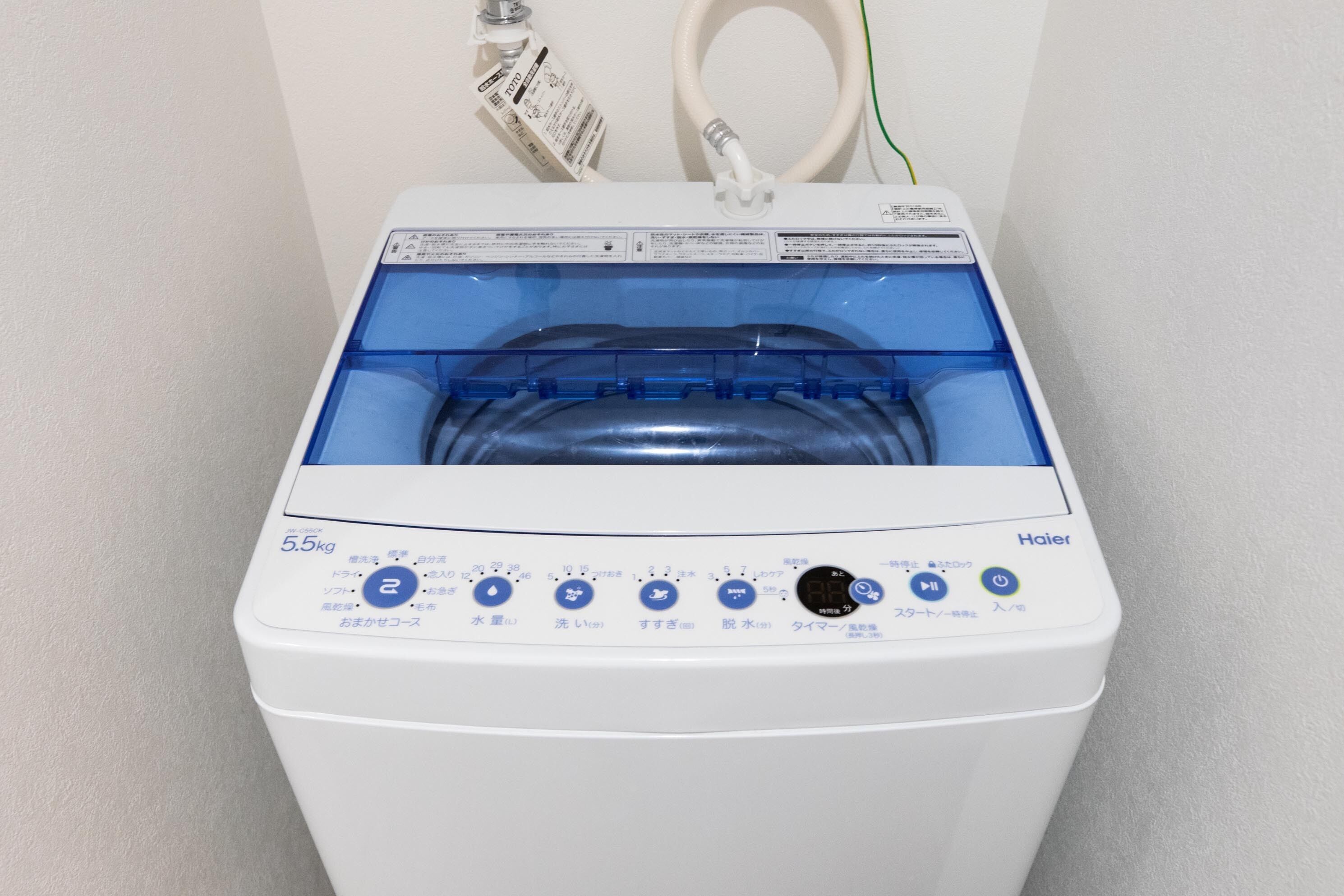 A white Haier washing machine with a transparent water tank, control panel with multiple settings, and a power cord plugged in.