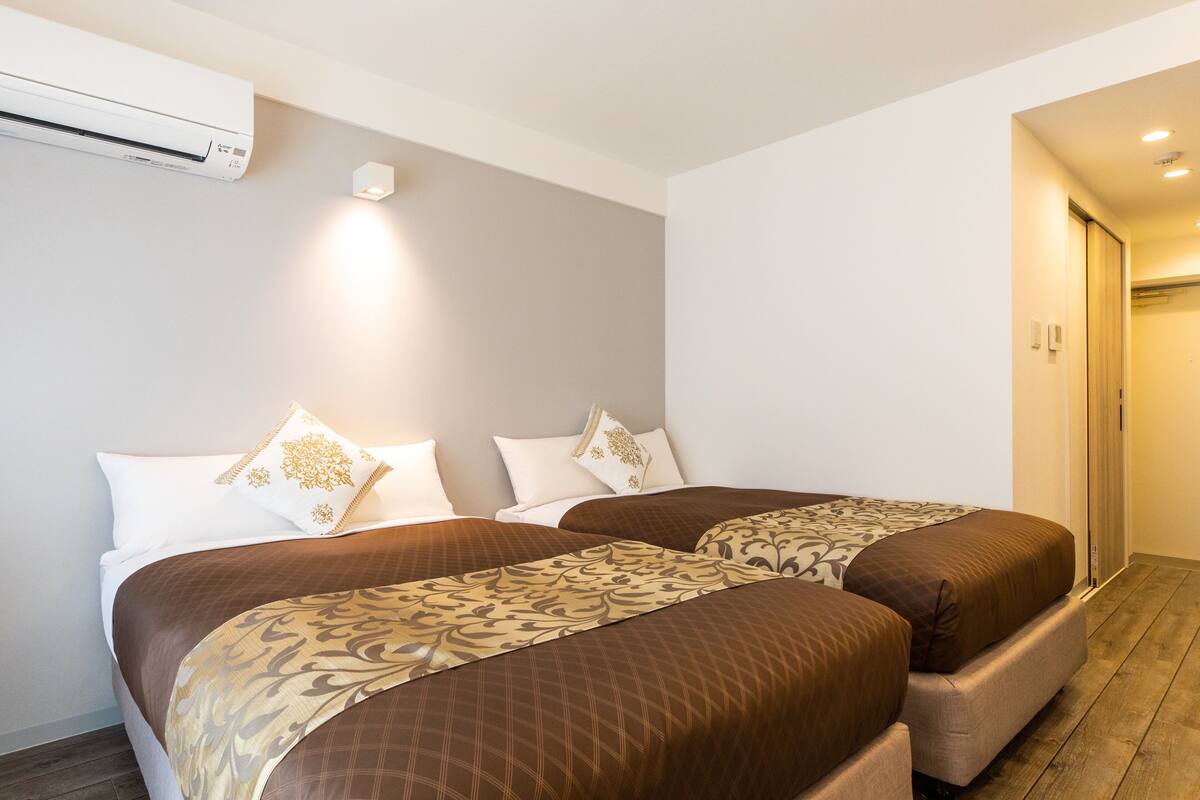 Quarto de hotel com duas camas, ar condicionado fixado na parede e porta que dá para outro quarto.