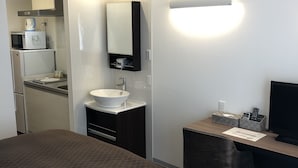 Habitación de hotel con cama, escritorio, computadora, lavamanos y microondas.