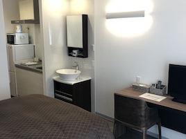 A hotel room with a bed, a desk with a computer, a sink, and a microwave.