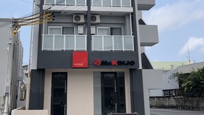 Un edificio de varios pisos con un diseño moderno, que cuenta con balcones y unidades de aire acondicionado en cada planta.