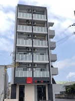 A multi-story building with a modern design, featuring balconies and air conditioning units on each floor.