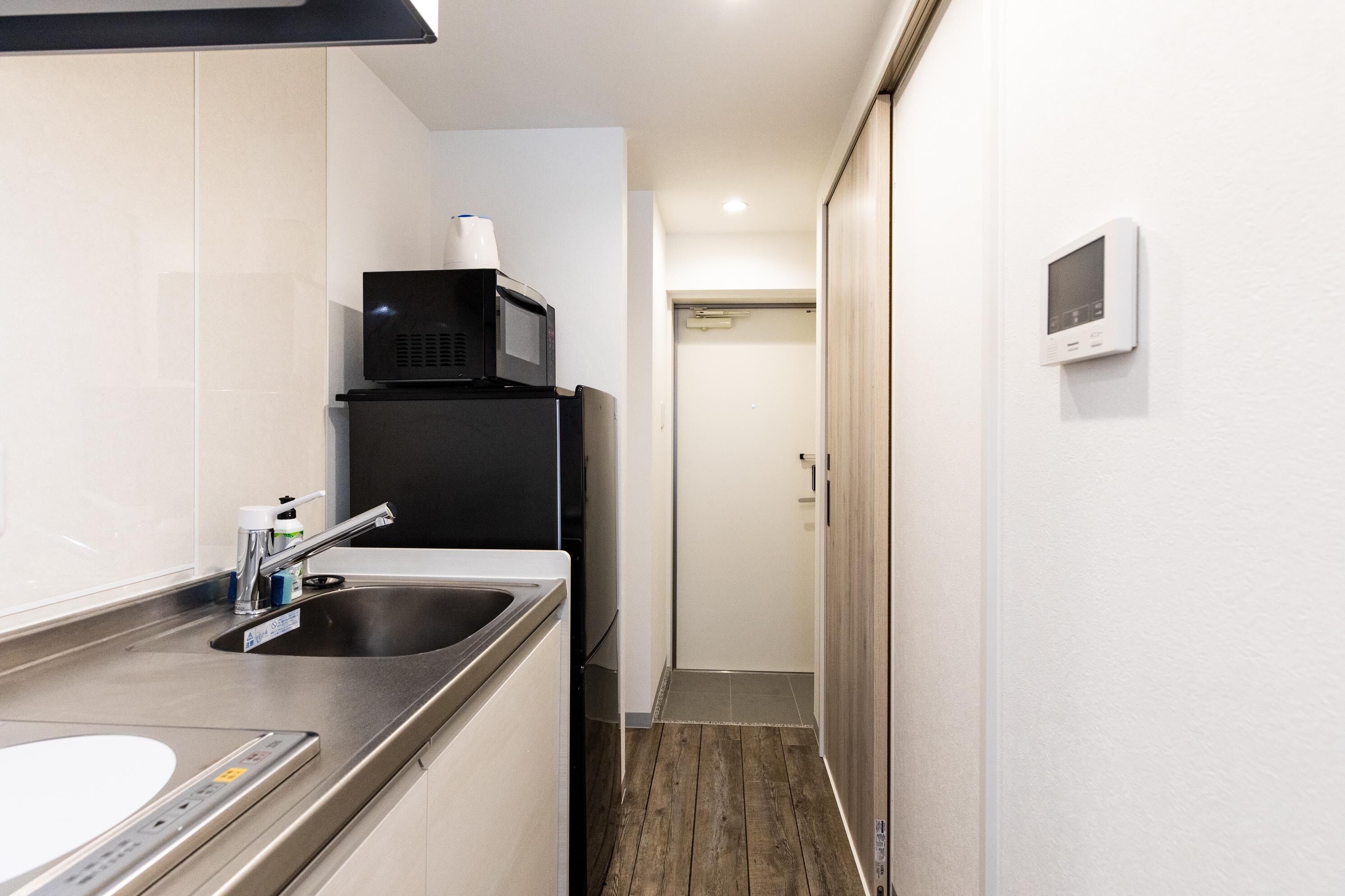 Una cocina compacta con un lavamanos de acero inoxidable, un microondas y un refrigerador pequeño.