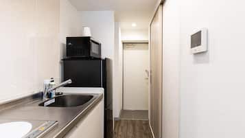 Una cocina compacta con un lavamanos de acero inoxidable, un microondas y un refrigerador pequeño.