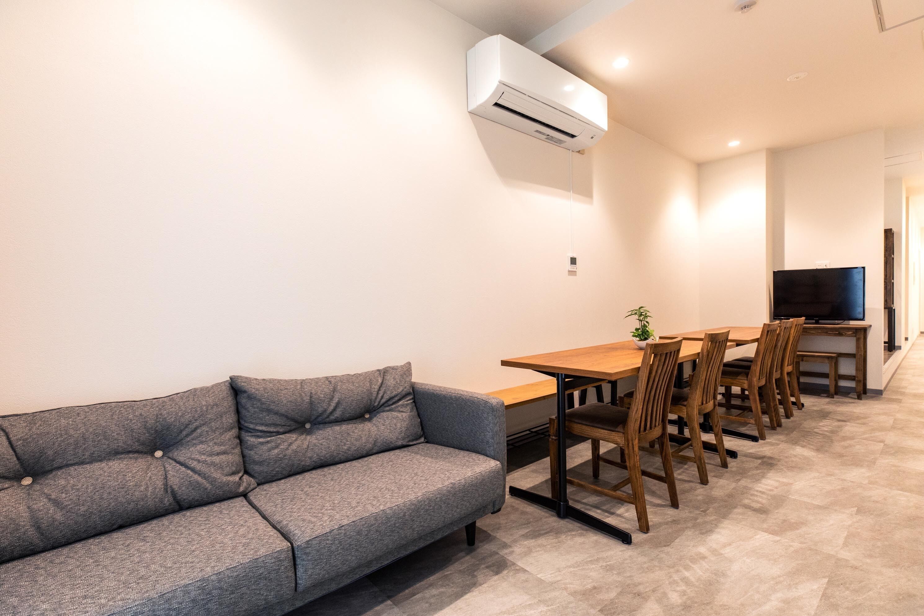 A modern living room with a grey sofa, a wooden dining table with chairs, and a flat-screen TV.