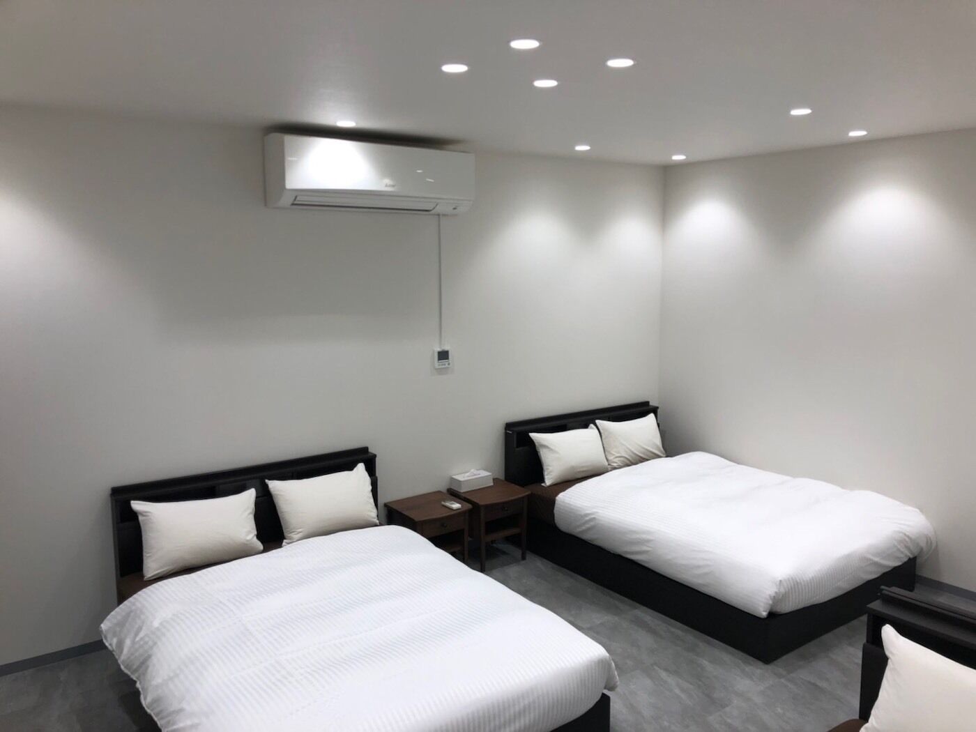 Ein modernes Hotelzimmer mit zwei Einzelbetten, einem Nachttisch, einem Schreibtisch und einer Wand-Klimaanlage.