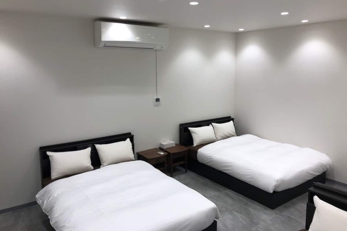 Quarto de hotel moderno com duas camas de solteiro, uma mesinha de cabeceira, uma escrivaninha e ar condicionado fixado na parede.