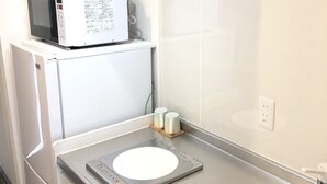 Una cocina compacta con microondas, un refrigerador pequeño, un lavamanos y una balanza en la encimera.