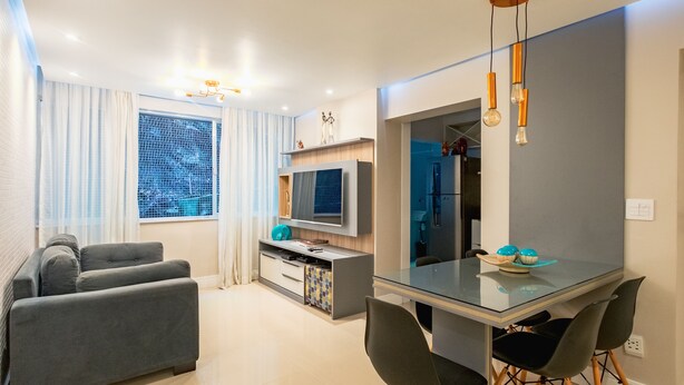 A modern living room with a sofa, a glass dining table with chairs, a TV, and a kitchen area. - Welcome Rio - Ipanema Beach - Posto 9 (Rio de Janeiro)