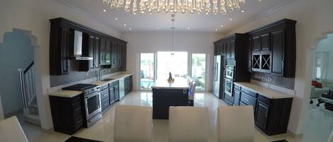 A modern kitchen with dark cabinetry, a central island, and a chandelier.