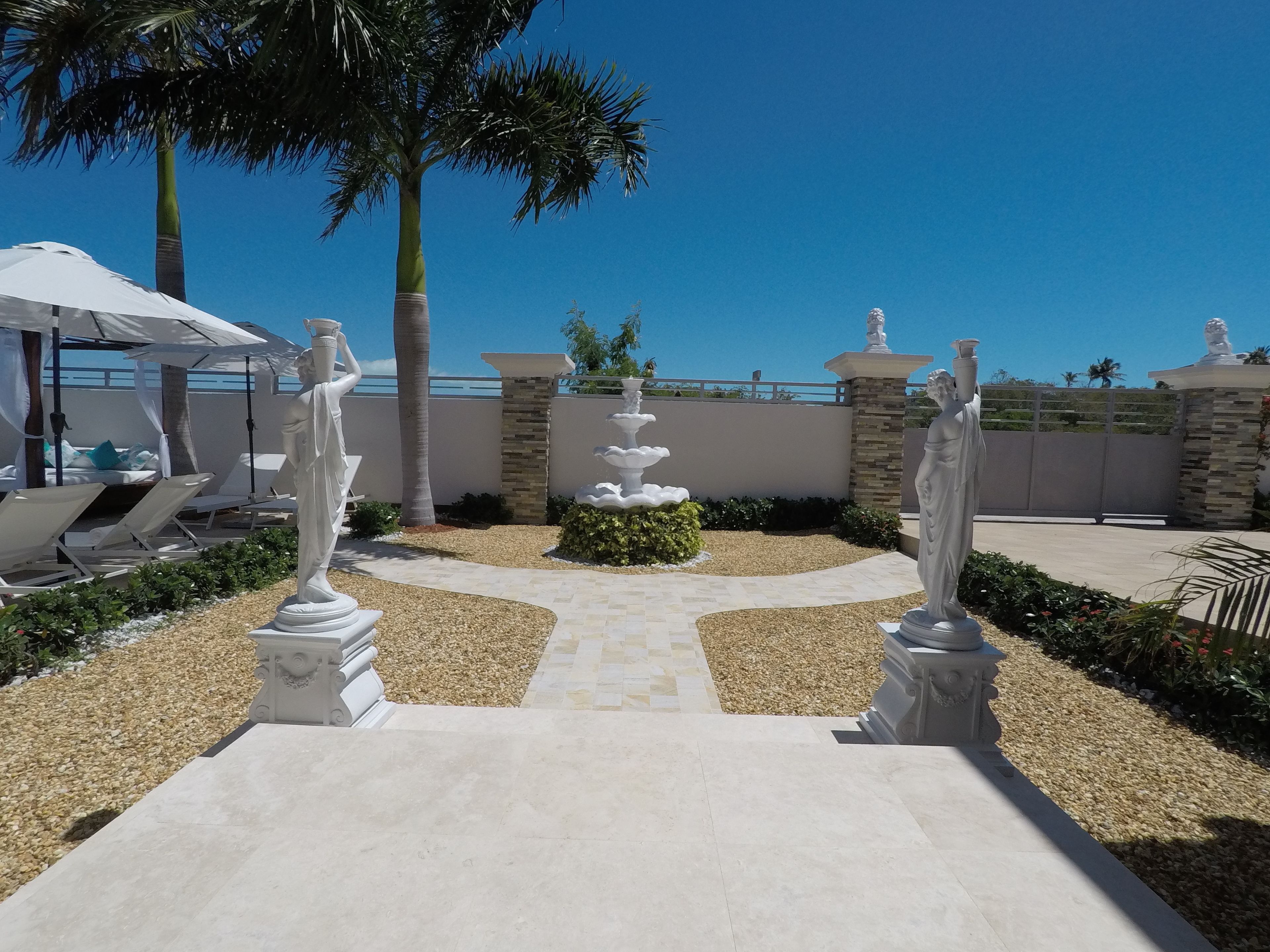 A pool area with white statues, a palm tree, and a clear blue sky.