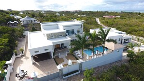 Una casa moderna de dos pisos con piscina, rodeada de vegetación exuberante y una vista despejada al océano.