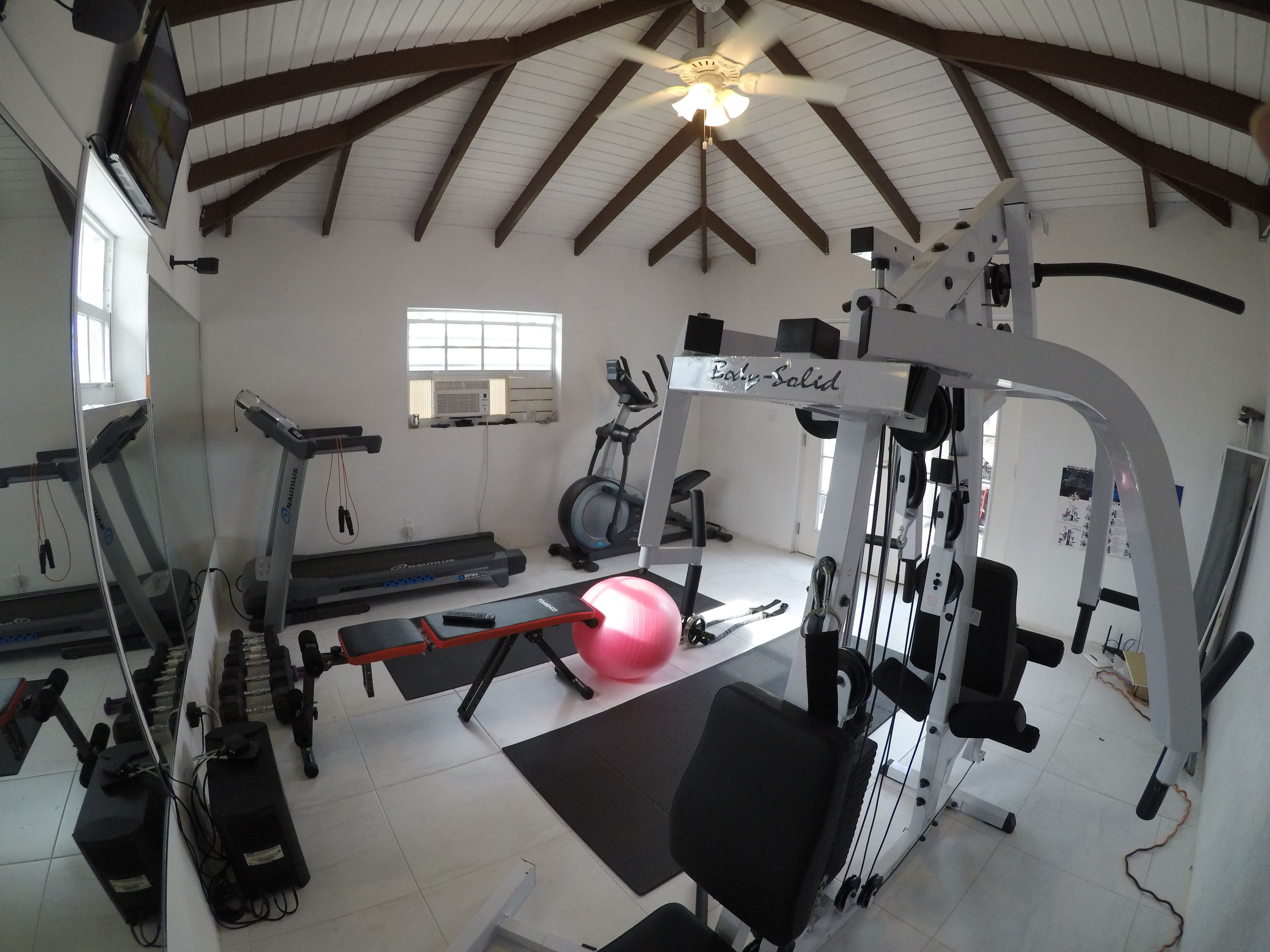 Un gimnasio con cintas de correr, elíptica, banca de pesas y máquina de poleas.