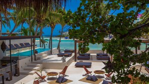 Un espace piscine aménagé dans un complexe hôtelier, avec des chaises longues, un toit de chaume et une vue sur la plage.