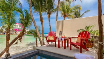 A poolside area with a view of the beach, red chairs, a small table with a candle, and a statue.