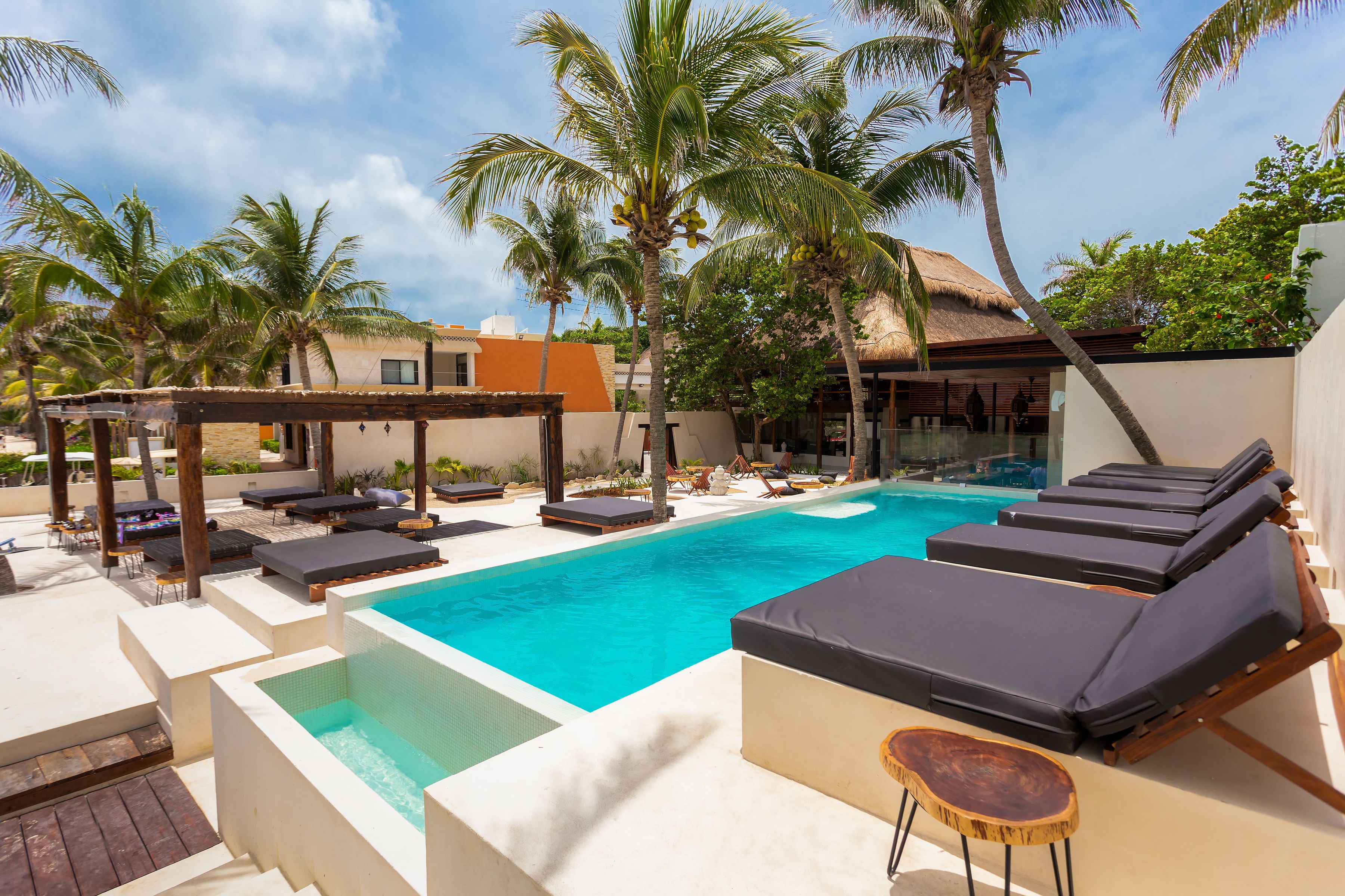 A pool area with lounge chairs, a hot tub, and palm trees.