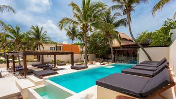 A pool area with lounge chairs, a hot tub, and palm trees.