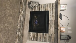 A stone fireplace with a black glass door, a decorative lantern, and a framed picture on the wall. - Perfect get away that is minutes from Legendary Downtown Sturgis! (Sturgis)