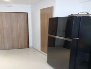 A room with a wooden door, a black refrigerator, and a white wall.