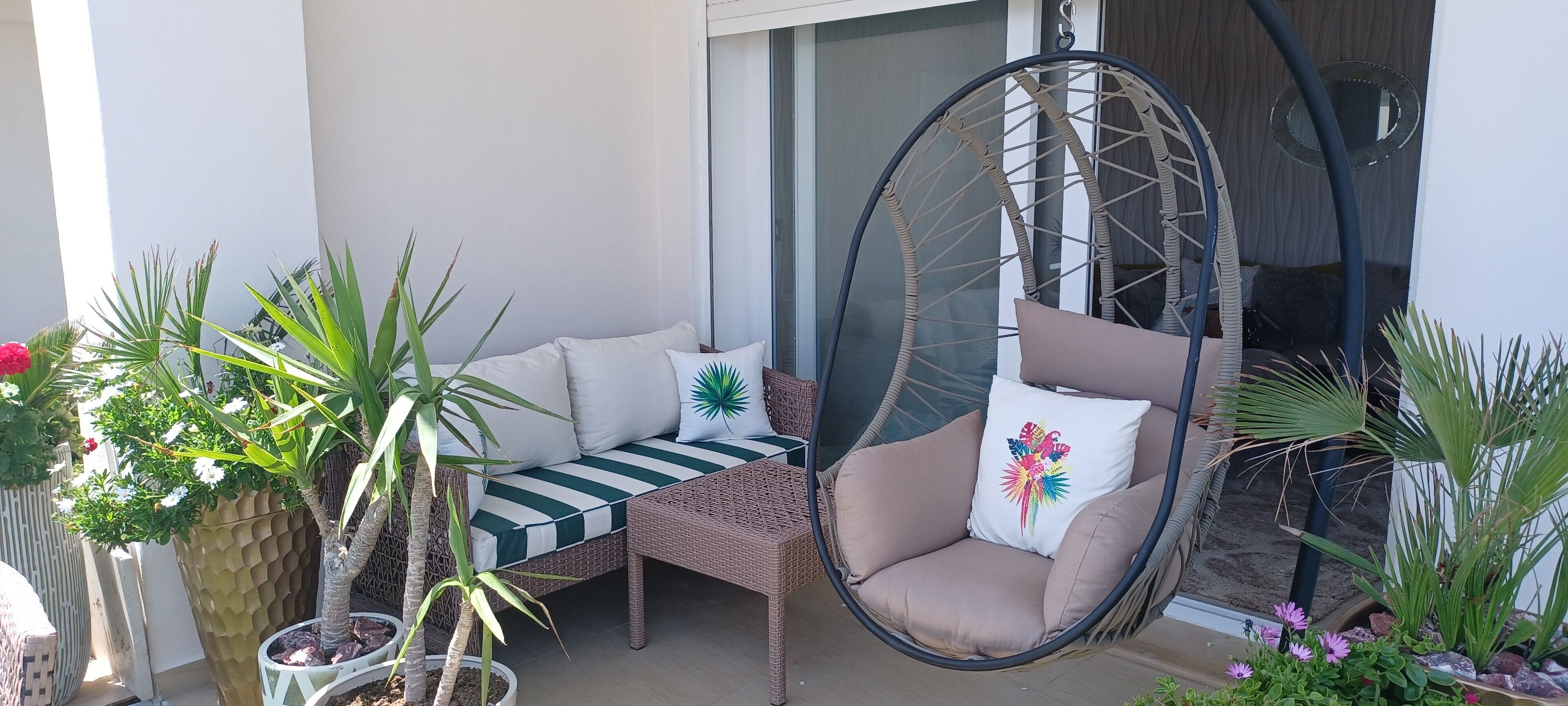 A balcony with a hanging chair, a cushioned bench, and potted plants.