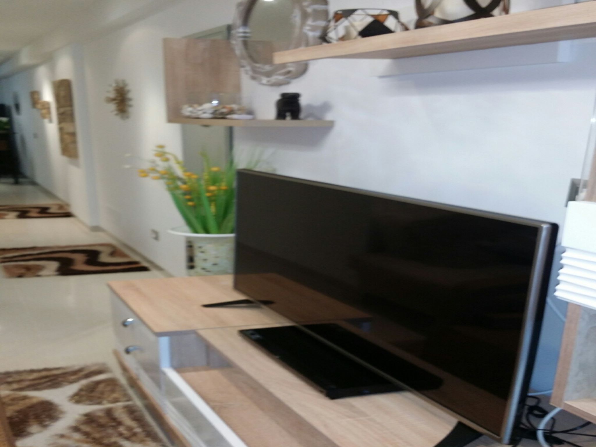 Una sala de estar moderna con un televisor de pantalla plana sobre un soporte de madera, una mesita con un control remoto y una planta decorativa.