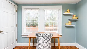A room with a wooden table and a patterned chair, a white door, and a window with blinds. There are three yellow rubber ducks on a shelf. - Insta Worthy Stay! - Fun in Downtown Raleigh! (Raleigh)