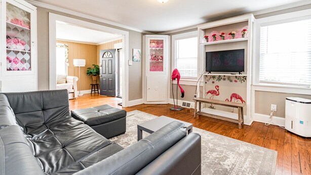 A living room with a grey sofa, a small table, and a bench. There is a door leading to another room, a lamp, and a white cabinet with pink flowers. - Insta Worthy Stay! - Fun in Downtown Raleigh! (Raleigh)