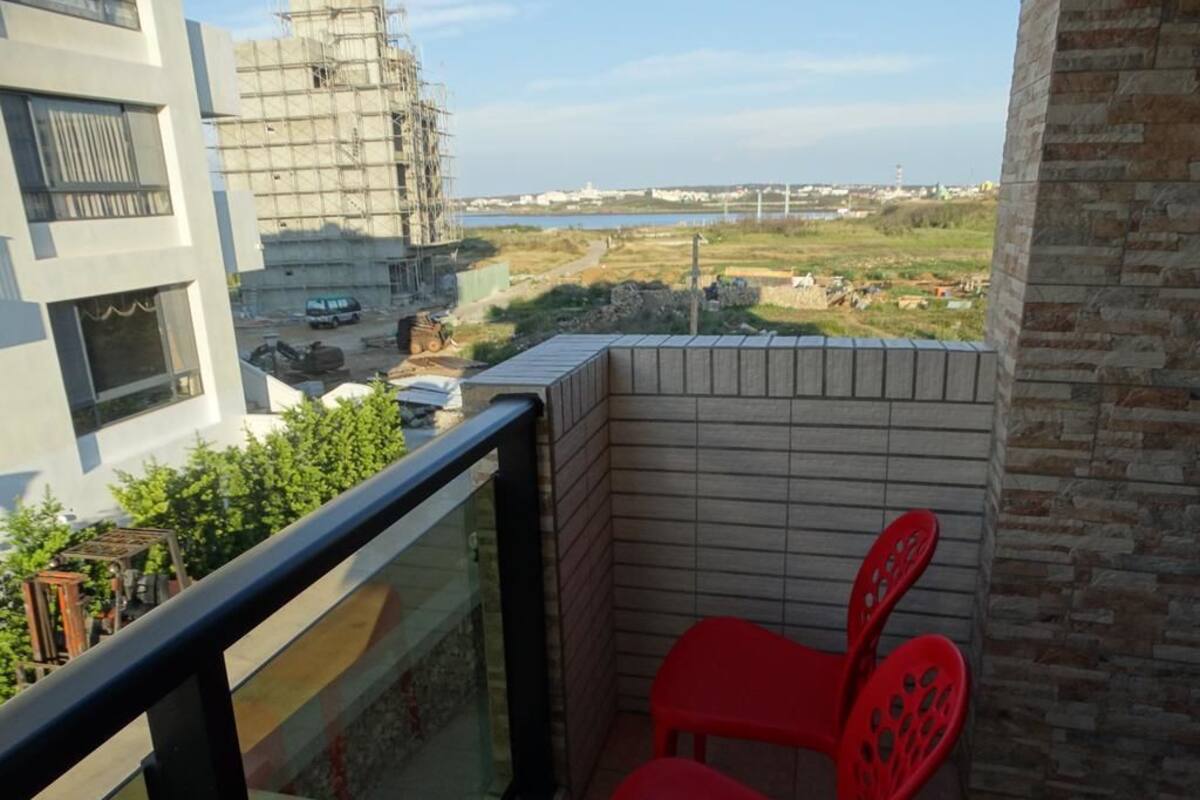 A balcony with a view of a construction site, a body of water, and a distant bridge.