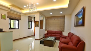 A spacious living room with a red sofa set, a glass-top coffee table, and a chandelier. - Chang Cheng Min Su (Magong)