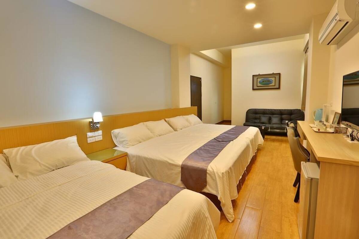 A hotel room with two beds, a desk, a chair, and a television.