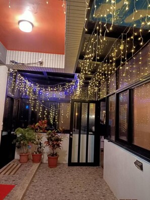 A corridor with string lights, potted plants, and a door leading to another area. - Chang Cheng Min Su (Magong)