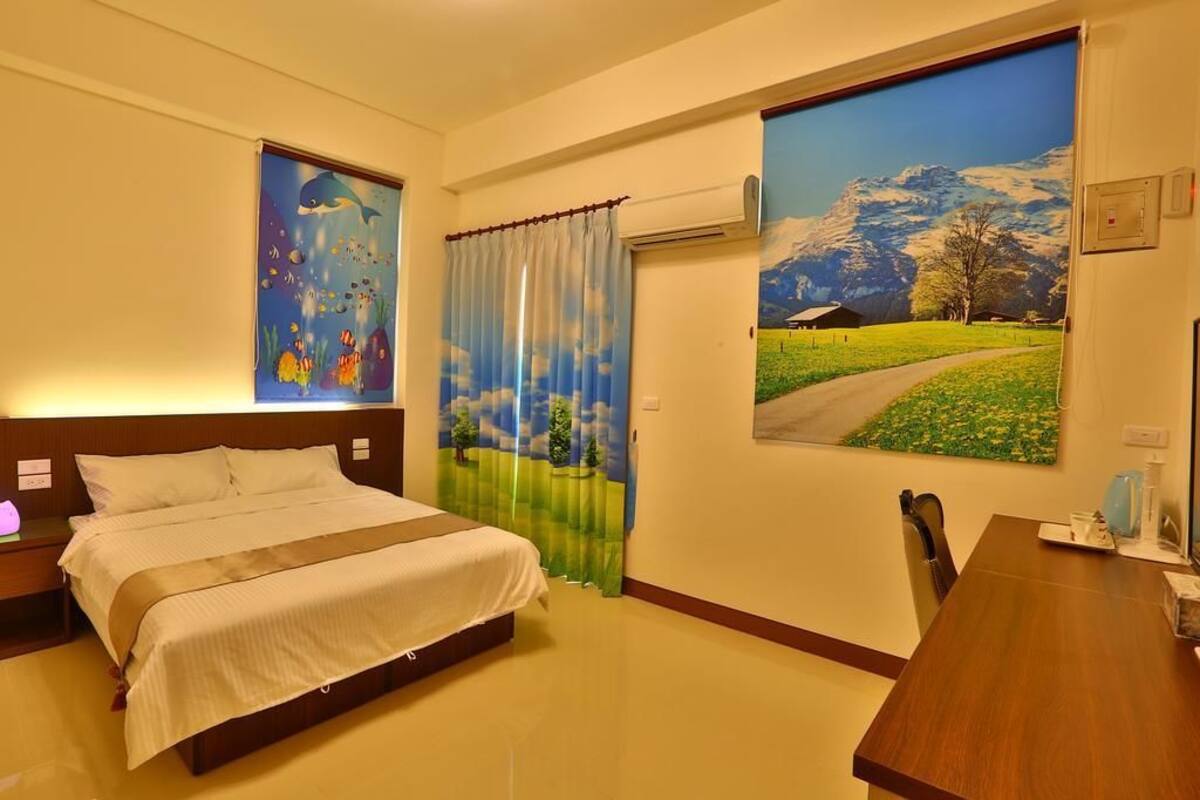 A hotel room with a bed, a desk, and two large wall art pieces depicting underwater scenes and a mountain landscape.