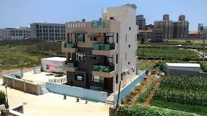 A multi-story building with balconies, a rooftop terrace with a table and chairs, and a garden area with crops. - Chang Cheng Min Su (Magong)