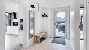 A modern, well-lit hallway with a wooden bench, a large mirror, and a door leading to a balcony.