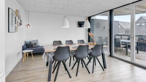 A modern dining area with a large table, black chairs, and pendant lighting.