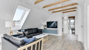A modern living room with a black leather sofa, a white coffee table, and a TV on a wooden stand.