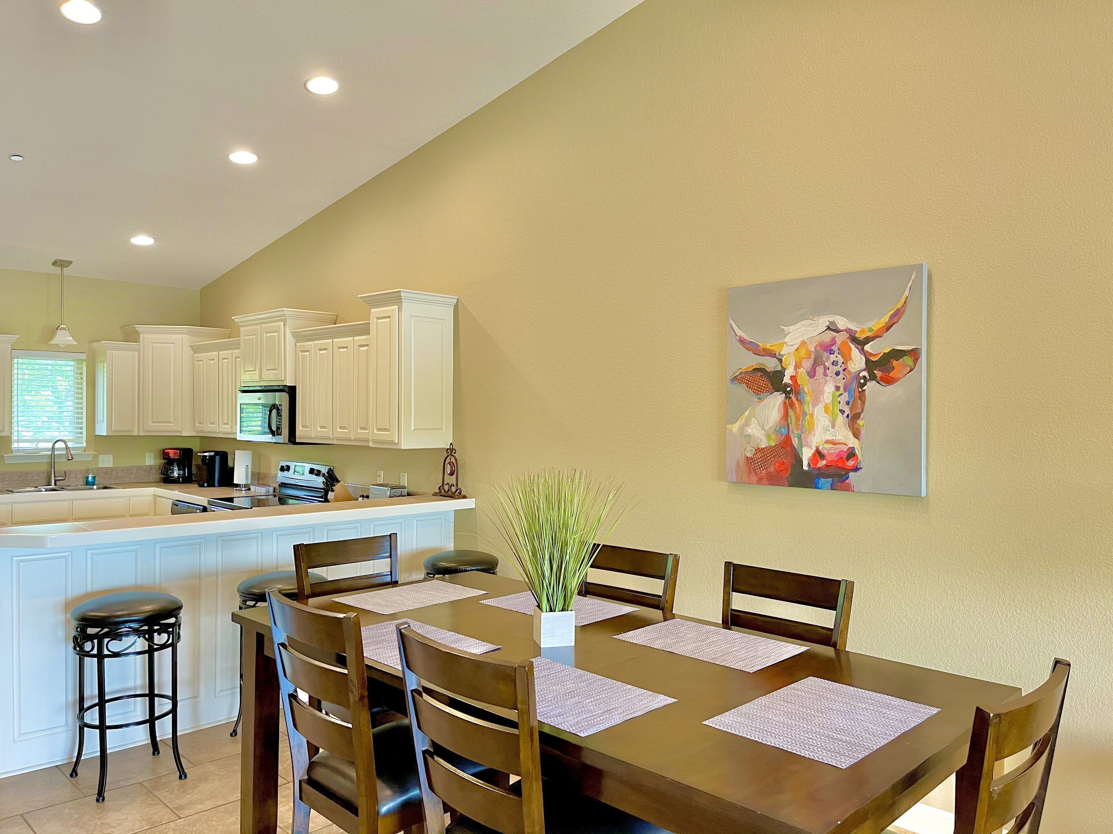 A dining area with a wooden table, chairs, and a vase with green plants.