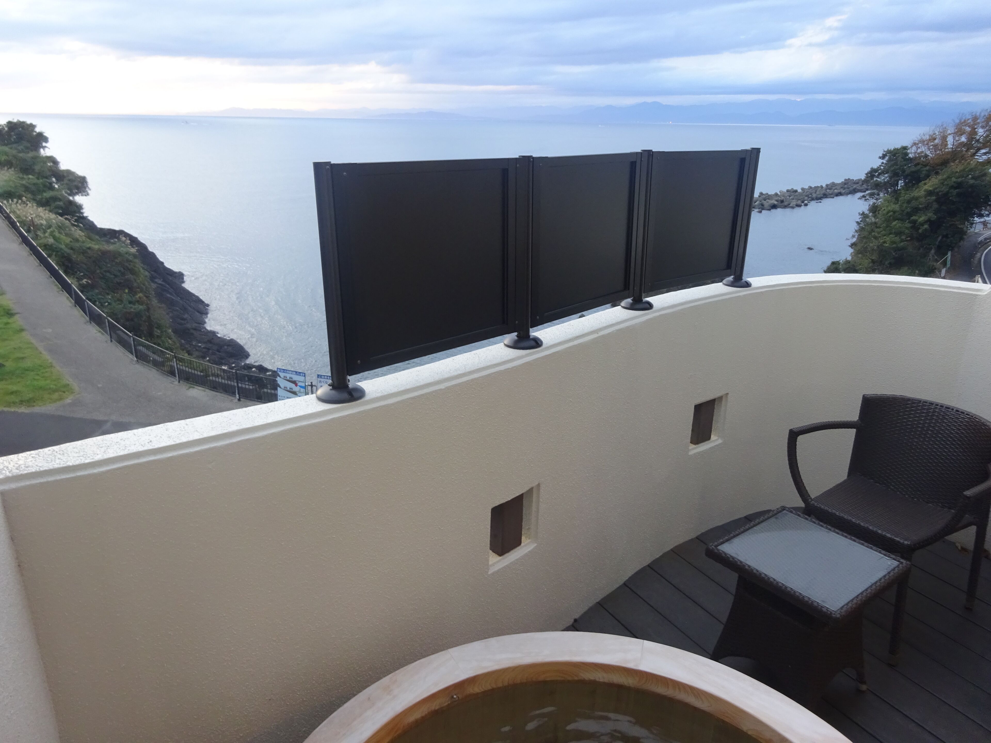 A balcony with a view of the sea, a small table, and a chair.