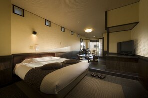 Habitación de hotel con una cama grande, un escritorio, un televisor y un baño visible a través de una puerta abierta.