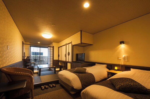 Quarto de hotel com duas camas, televisão, escrivaninha e vista para o exterior.