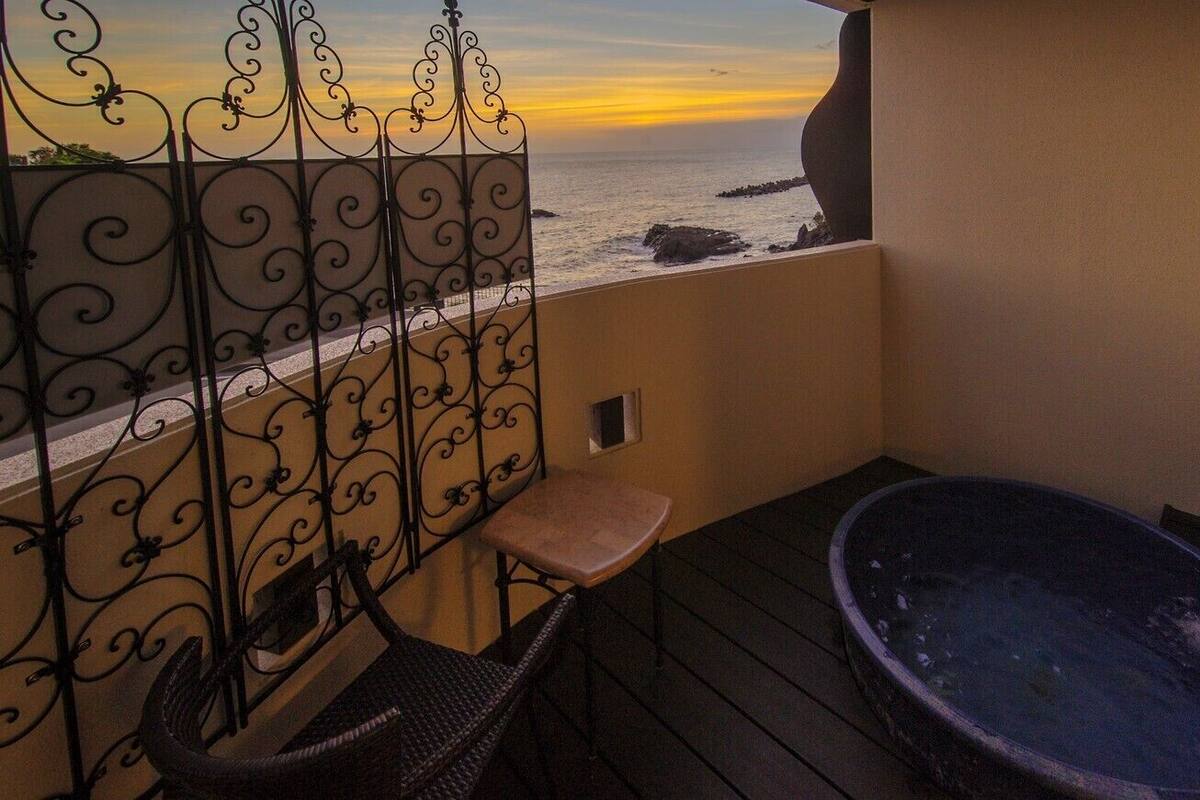 A balcony with a wrought iron railing, a hot tub, and a chair.
