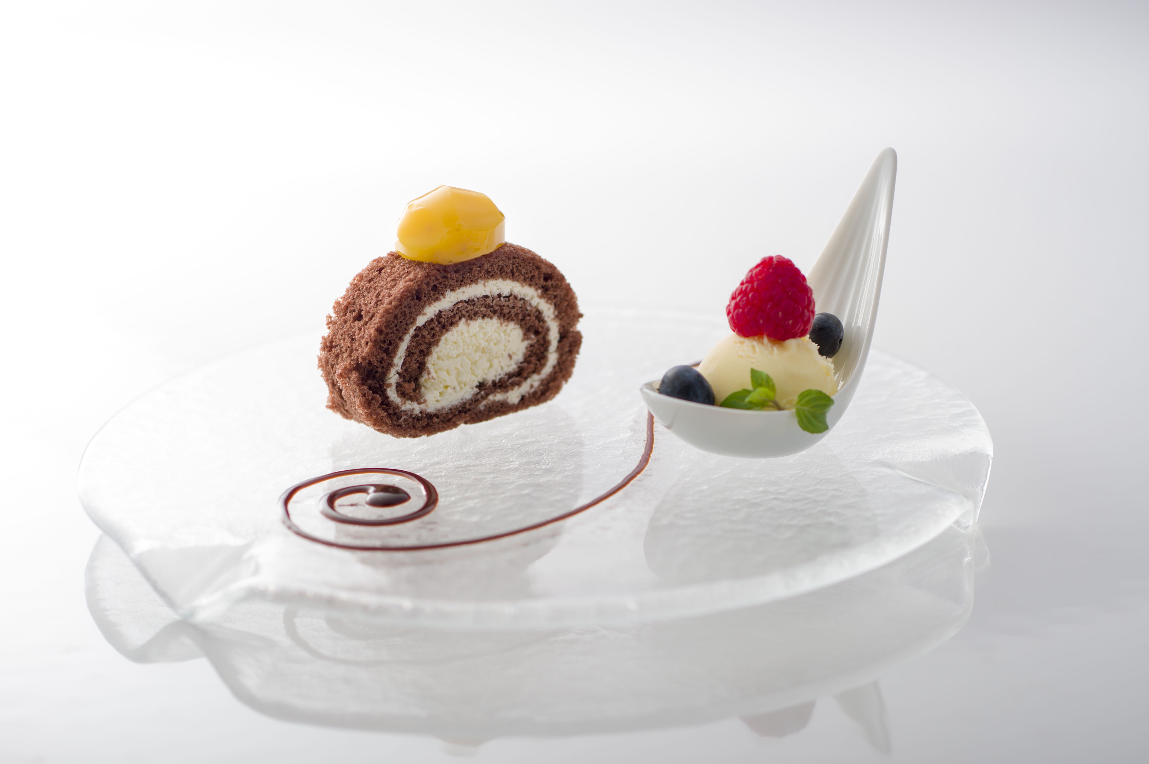 A dessert with a rolled cake, a scoop of ice cream, and fresh berries on a white plate.
