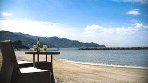 A beachside table with chairs and a bottle of wine, overlooking a calm sea and distant mountains. - Hoozue No Toki (Izu)