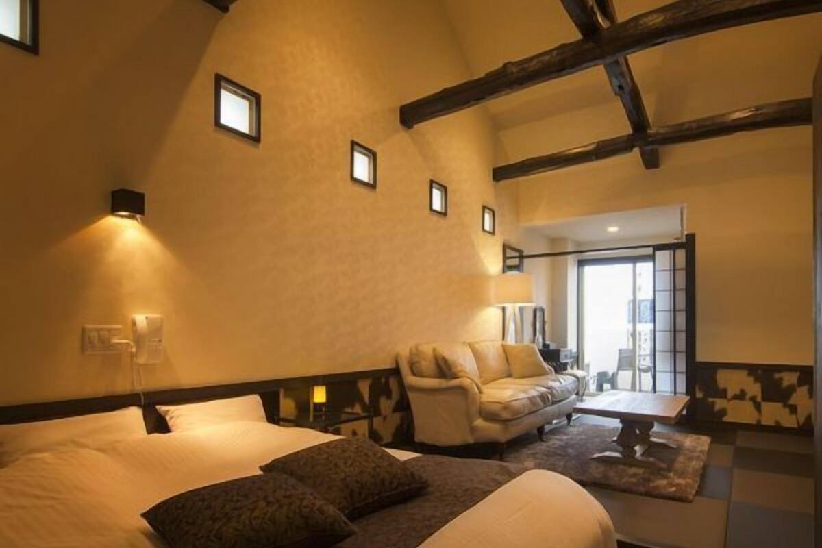 A bedroom with a large bed, a sofa, a small table, and a view of the outside.